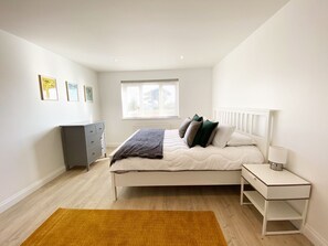 A bedroom with a bed, bedside table, nightstand, dresser, window, and artwork on the wall.