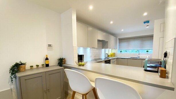 A modern kitchen with white cabinets, a central island with bar stools, and a built-in oven. - NEW FOR 2020 - 3 Harvest Moon is a stunning fully refurbished 2 bedroom, 2 en suite bathroom apartme (Newquay)