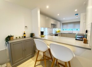 A modern kitchen with white cabinets, a central island with bar stools, and a built-in oven.