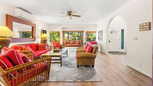 A spacious living room with wicker furniture, a ceiling fan, and large windows offering a view of the outdoors. - Spacious Poipu Beach Home near Hyatt-Remodeled Kitchen & Bathrooms Large Hot Tub (Koloa)