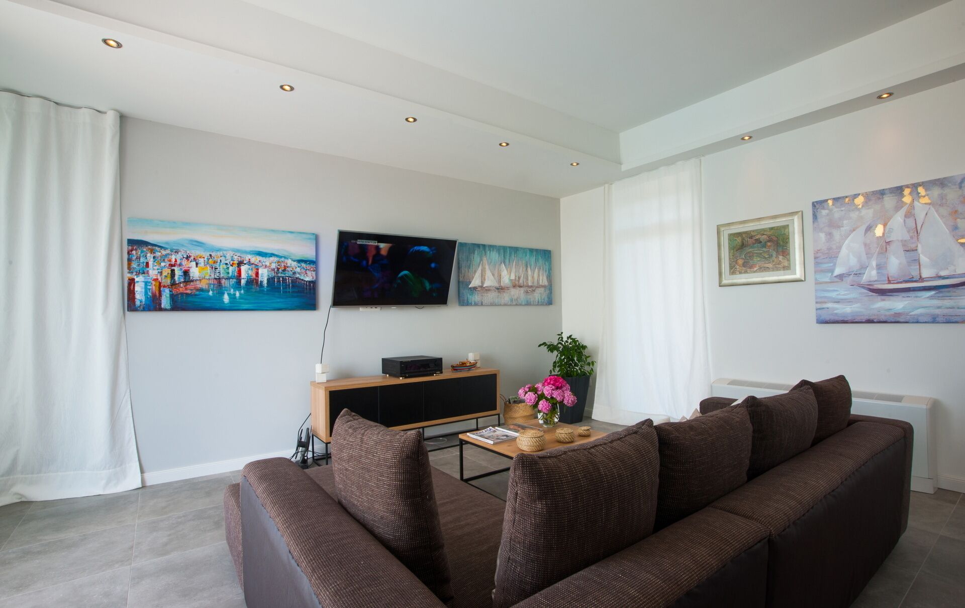 A living room with a brown sofa, a flat-screen TV, and artwork on the walls.