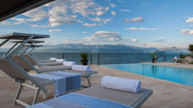 Ein Poolbereich mit Liegestühlen und Handtüchern, mit Blick auf ein Gewässer und Berge.