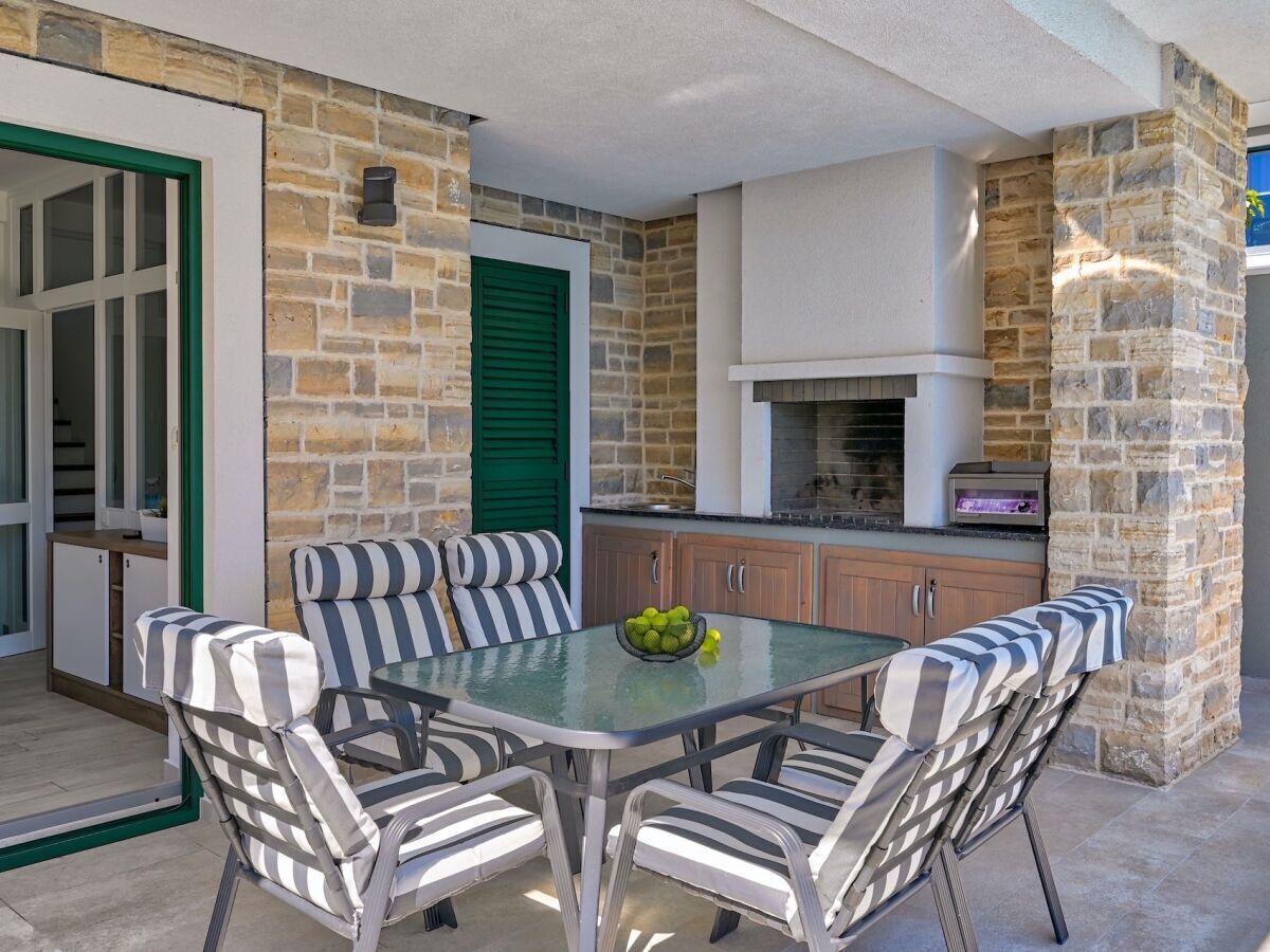 An outdoor kitchen area with a stone wall, a built-in grill, and striped outdoor furniture.