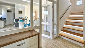 Un interior moderno con una escalera, un comedor y vistas a través de puertas de cristal.