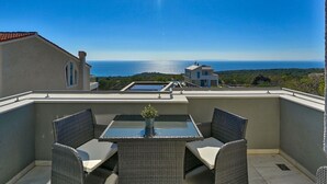 Un balcón con mobiliario de mimbre, una mesa de vidrio y vistas al mar.