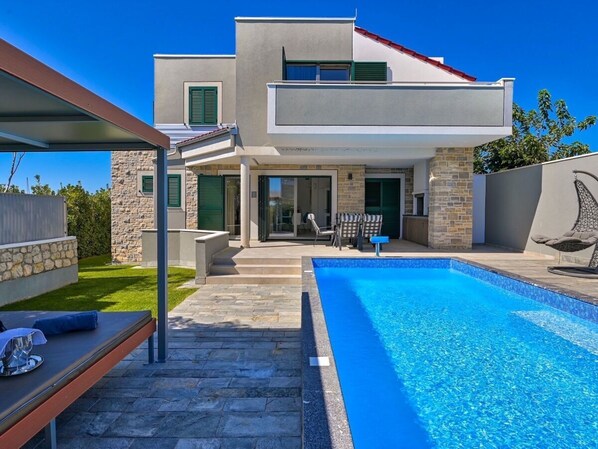 A modern two-story house with a swimming pool, stone exterior, and a covered patio area.