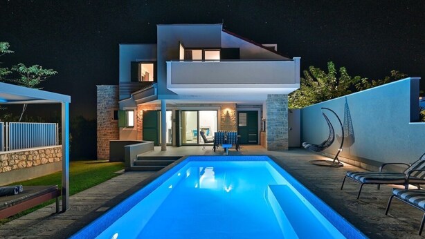 Una casa moderna de dos pisos con piscina, mobiliario exterior y una zona de patio bien iluminada.