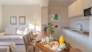 Una cocina moderna con armarios blancos, un comedor con mesa de madera y una sala de estar con sofá y sillones.