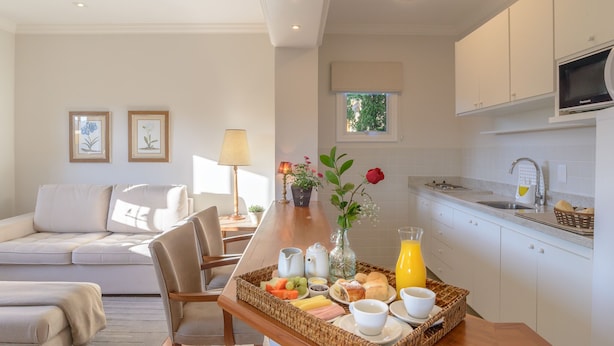 A modern kitchen with white cabinets, a dining area with a wooden table, and a living room with a sofa and chairs. - Pousada La Bas Suites de Montagne (Campos do Jordão)