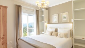 A bedroom with a large bed, a chandelier, a window with curtains, and framed pictures on the wall. - Pousada La Bas Suites de Montagne (Campos do Jordão)