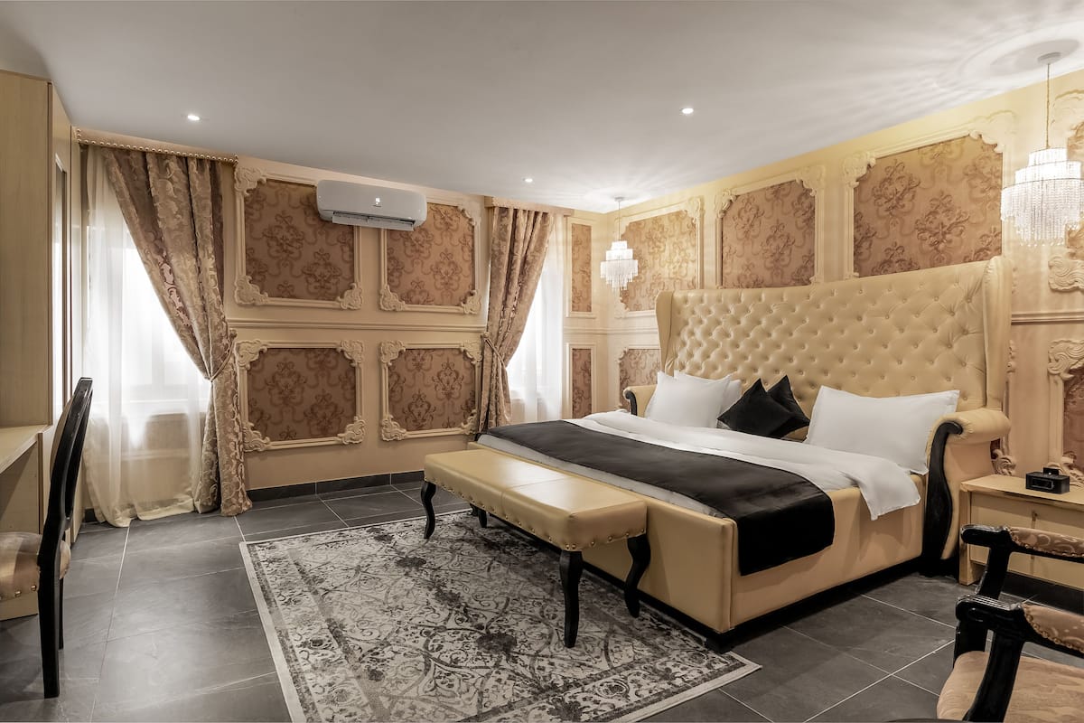 A luxurious bedroom with a large bed, a bench, a chandelier, and ornate wall paneling.