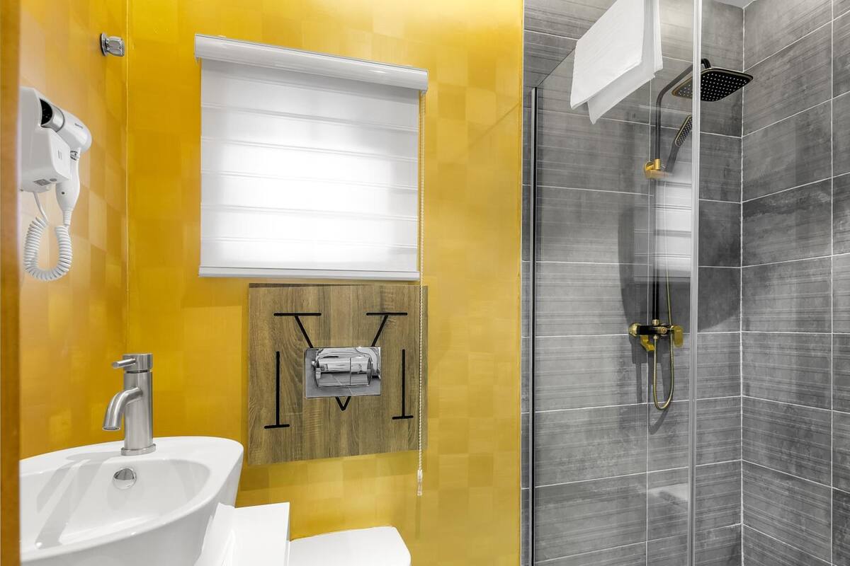 A modern bathroom with a yellow and grey color scheme, featuring a sink, toilet, and a glass-enclosed shower area.