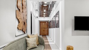 A hallway with a grey sofa, wooden door, and a TV mounted on the wall. - Villa Monument Hotel (Lagos)