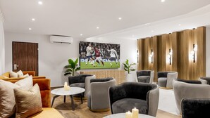 A modern living room with a large flat-screen TV, comfortable seating, and a wooden accent wall. - Villa Monument Hotel (Lagos)