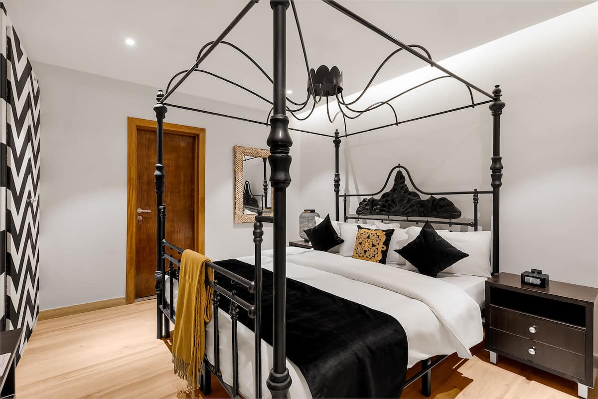 A four-poster bed with a canopy, a bedside table, a nightstand, and a wooden door.