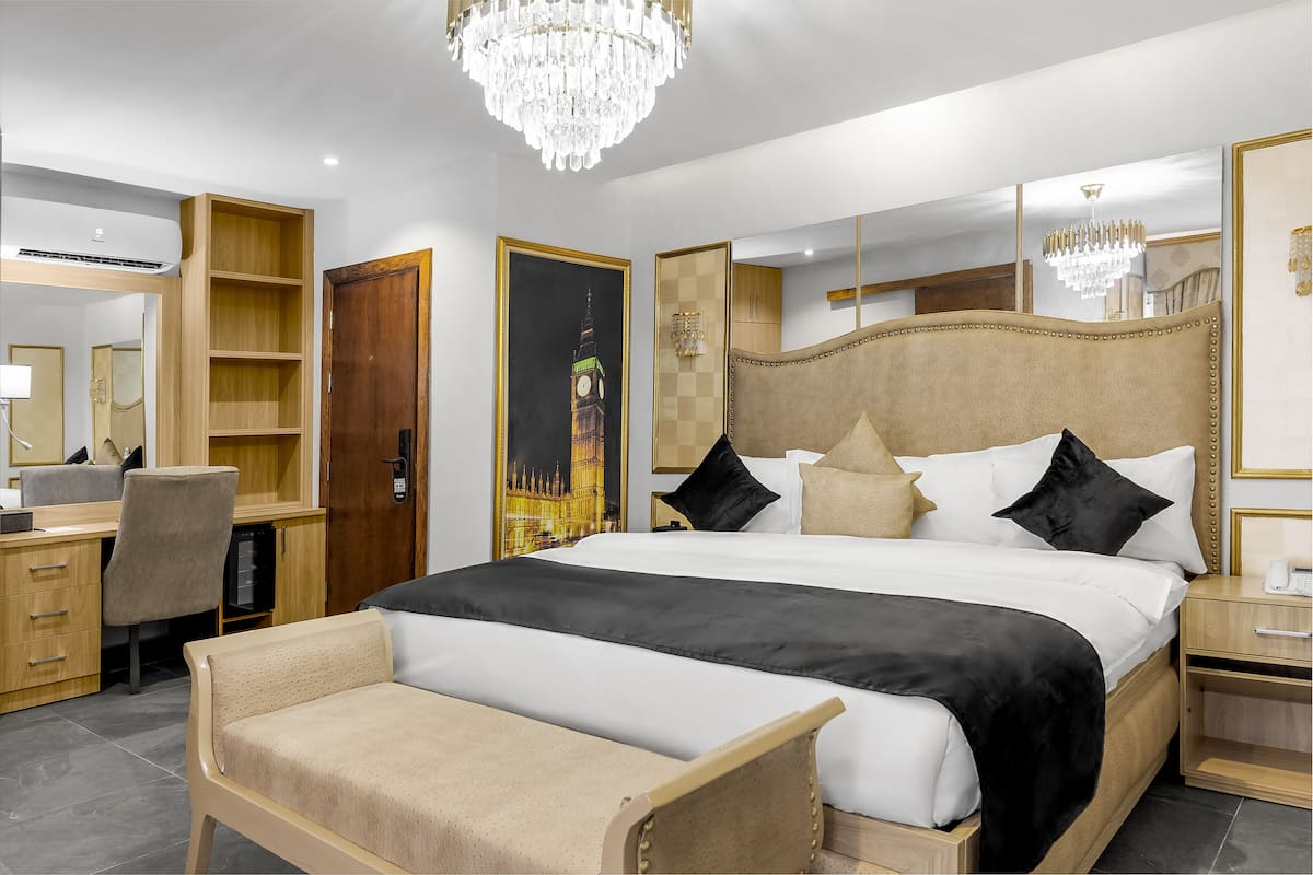 A modern hotel room with a large bed, a desk, a chair, a wardrobe, and a mirror.