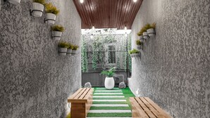 A narrow corridor with a wooden ceiling, white walls, and a green artificial turf path leading to a black gate. - Villa Monument Hotel (Lagos)