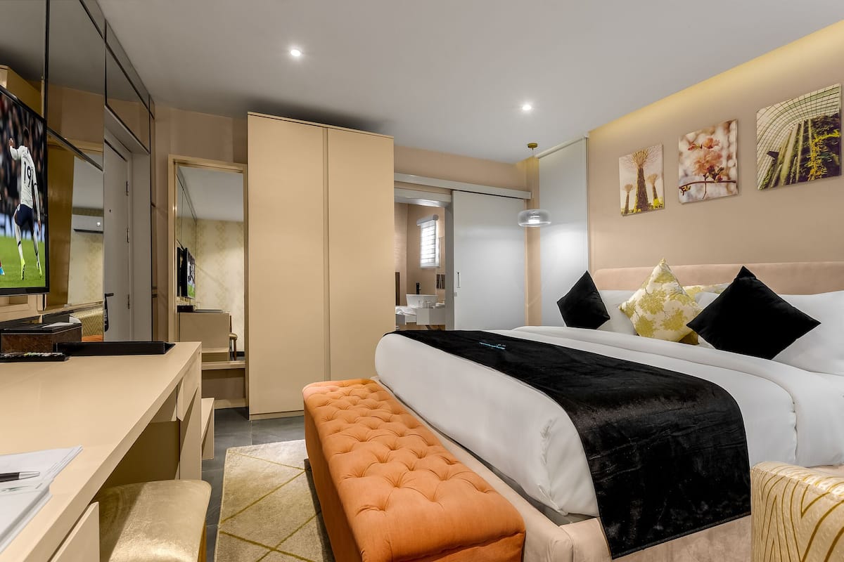 A modern hotel room with a bed, a desk, and a bench. There is a TV on the desk and a door leading to the bathroom.