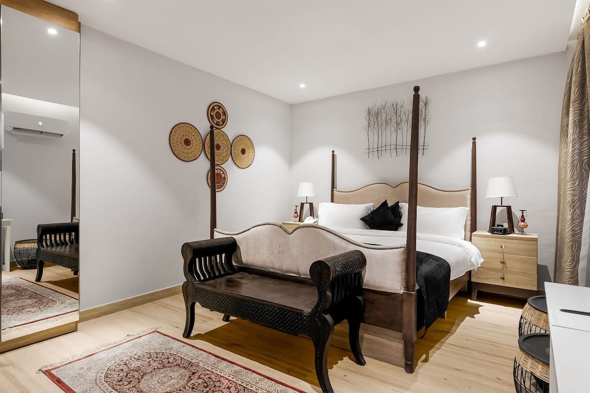 A four-poster bed with a wooden headboard, a bedside table with a lamp, and a mirror on the wall.