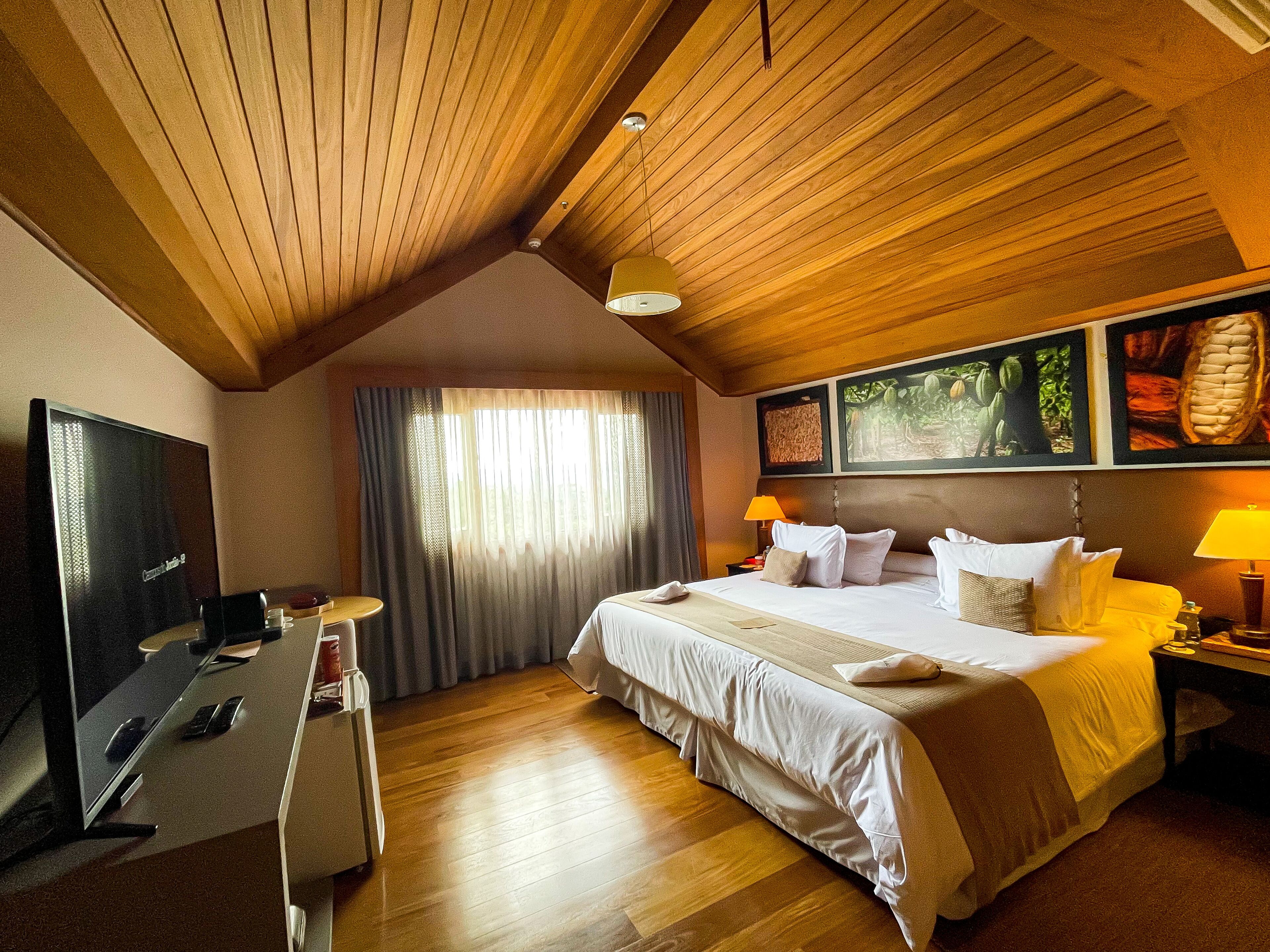 Ein Hotelzimmer mit einem großen Bett, einem Schreibtisch mit Fernseher und einem Fenster mit Vorhängen.