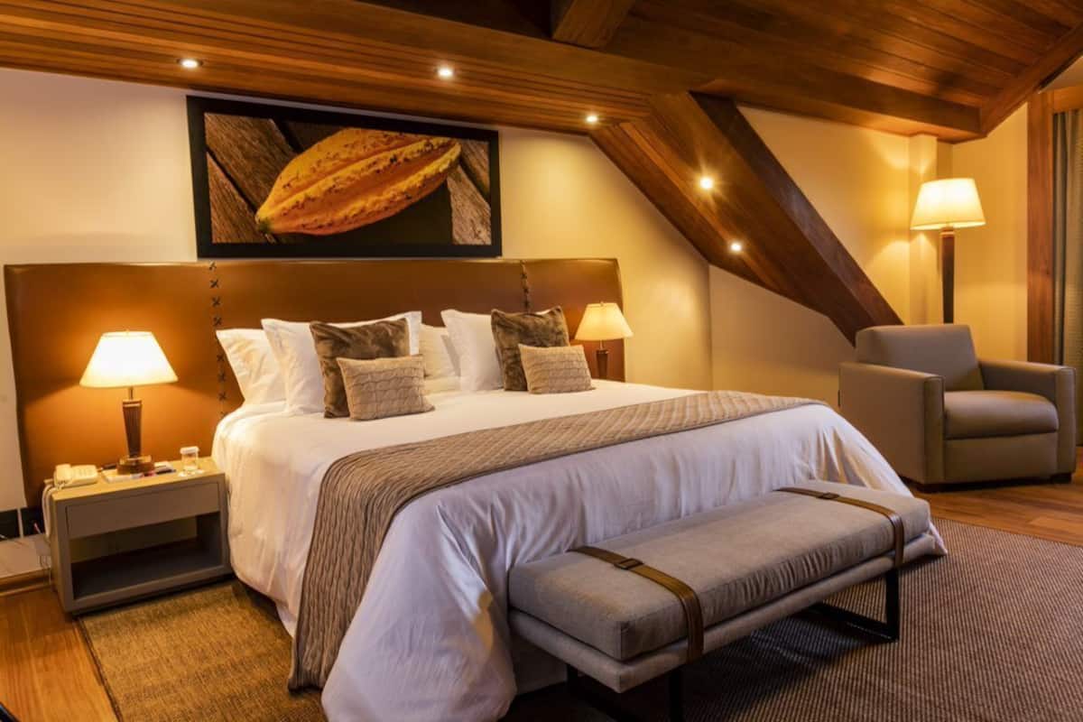A hotel room with a large bed, two bedside lamps, a chair, and a bench.