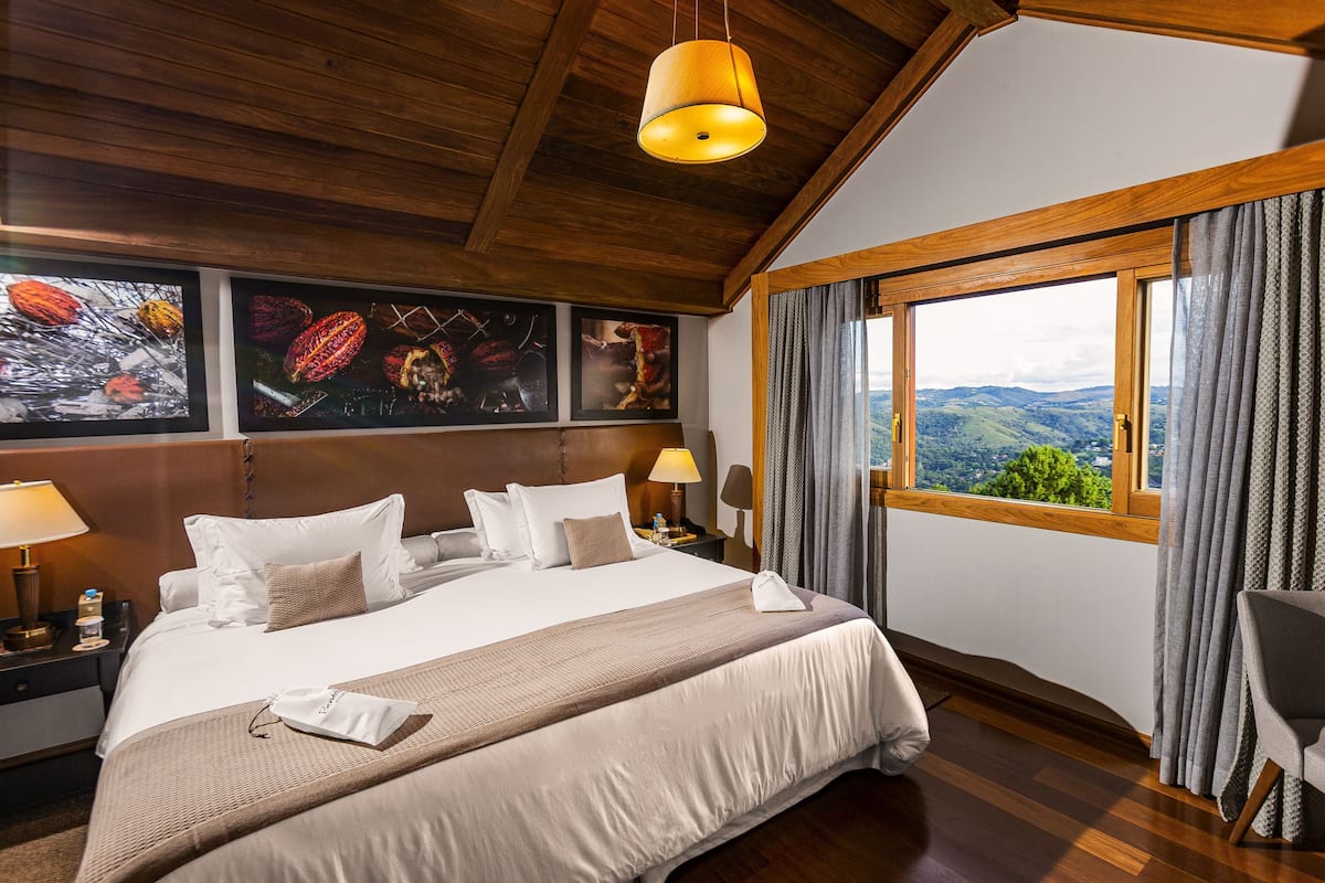 A hotel room with a large bed, wooden ceiling, a view through a window, and artwork on the wall.