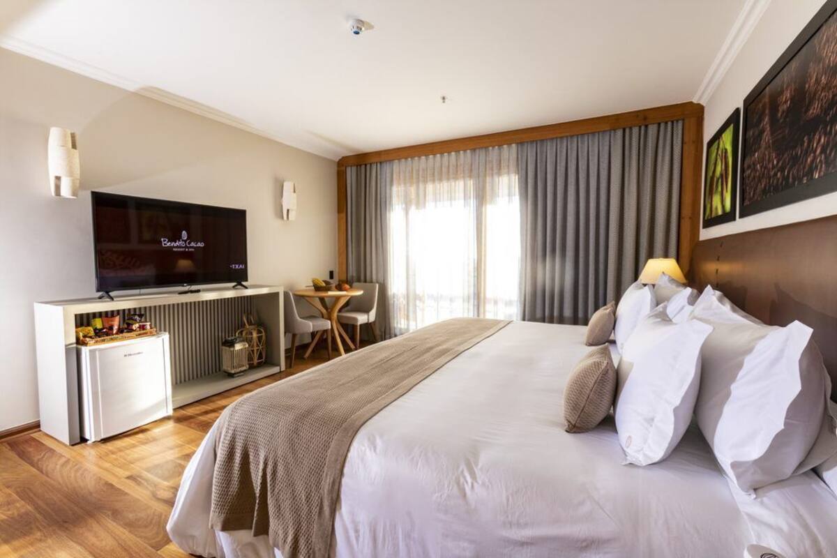A hotel room with a large bed, a television, a desk, and a window with curtains.