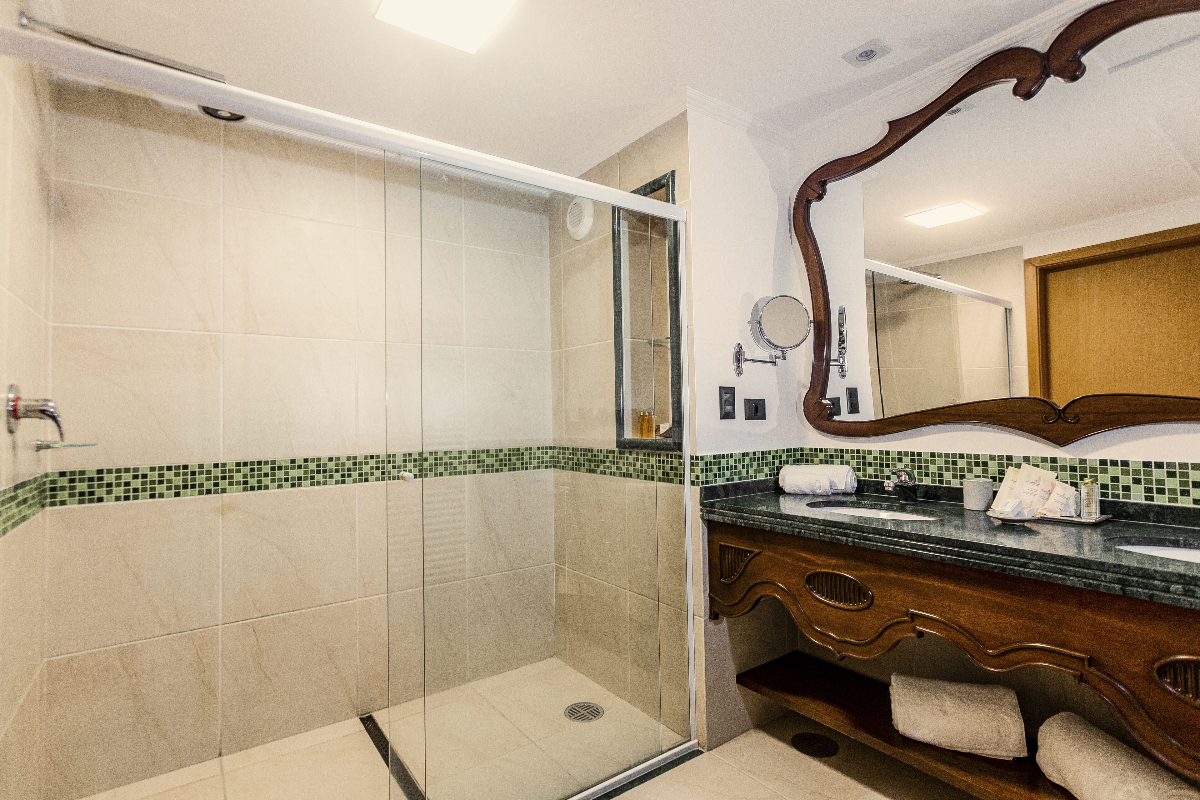Une salle de bain avec une douche à parois de verre, un meuble-lavabo en bois avec un miroir et un sol carrelé.