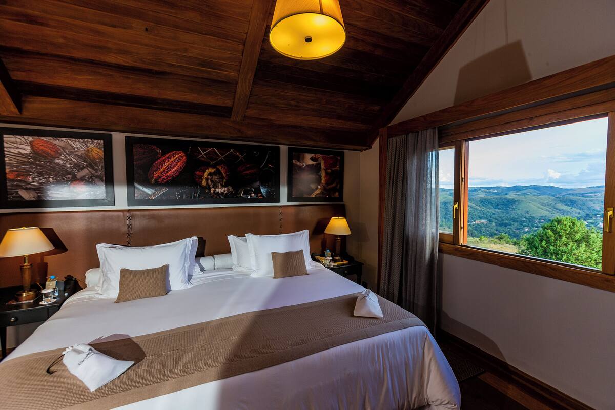 A hotel room with a large bed, wooden ceiling, and a view of the countryside.