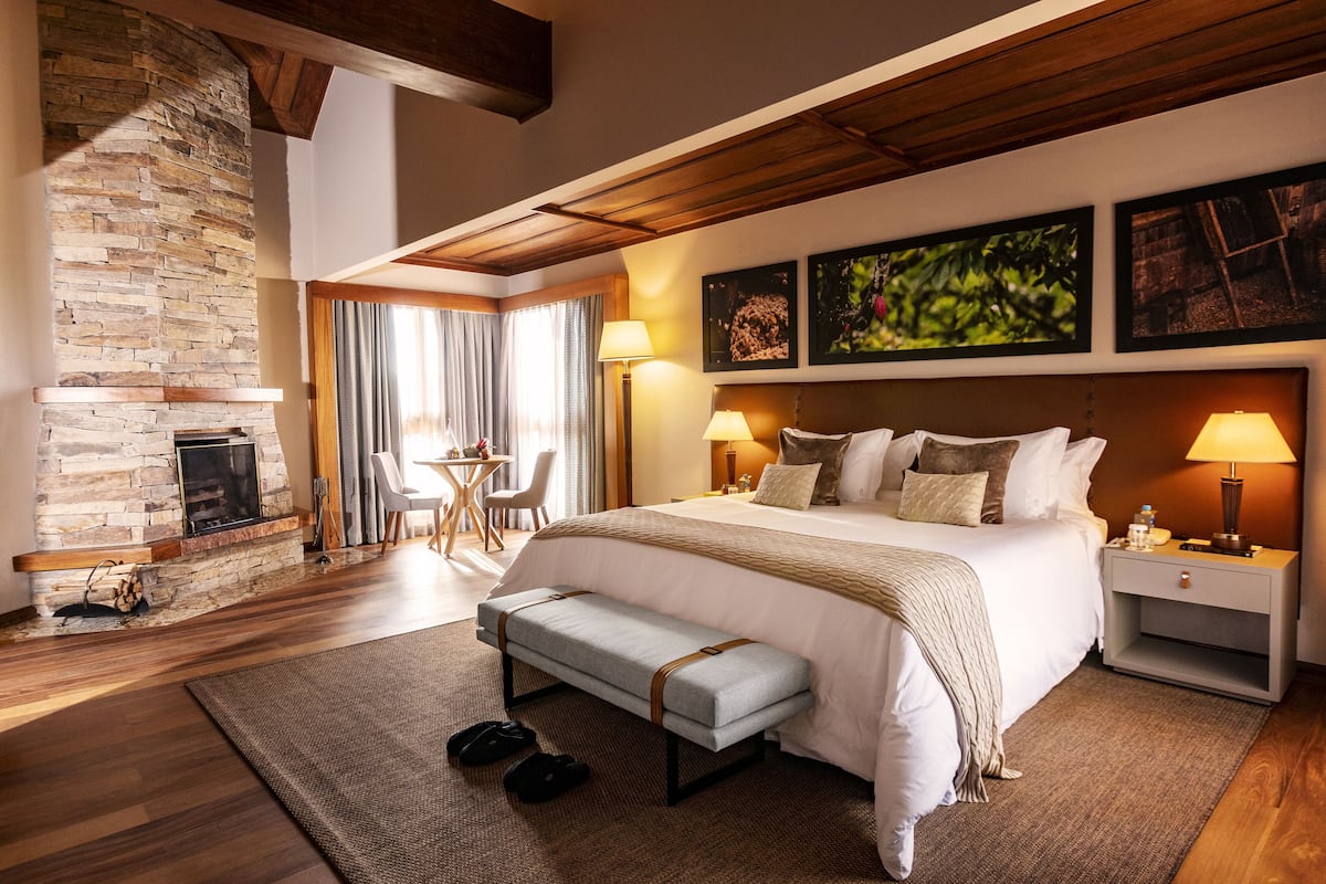 A spacious bedroom with a stone fireplace, a large bed, bedside lamps, and a bench.