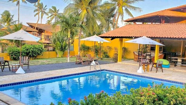 Piscina con sillas de descanso y sombrillas, rodeada de follaje y palmeras.