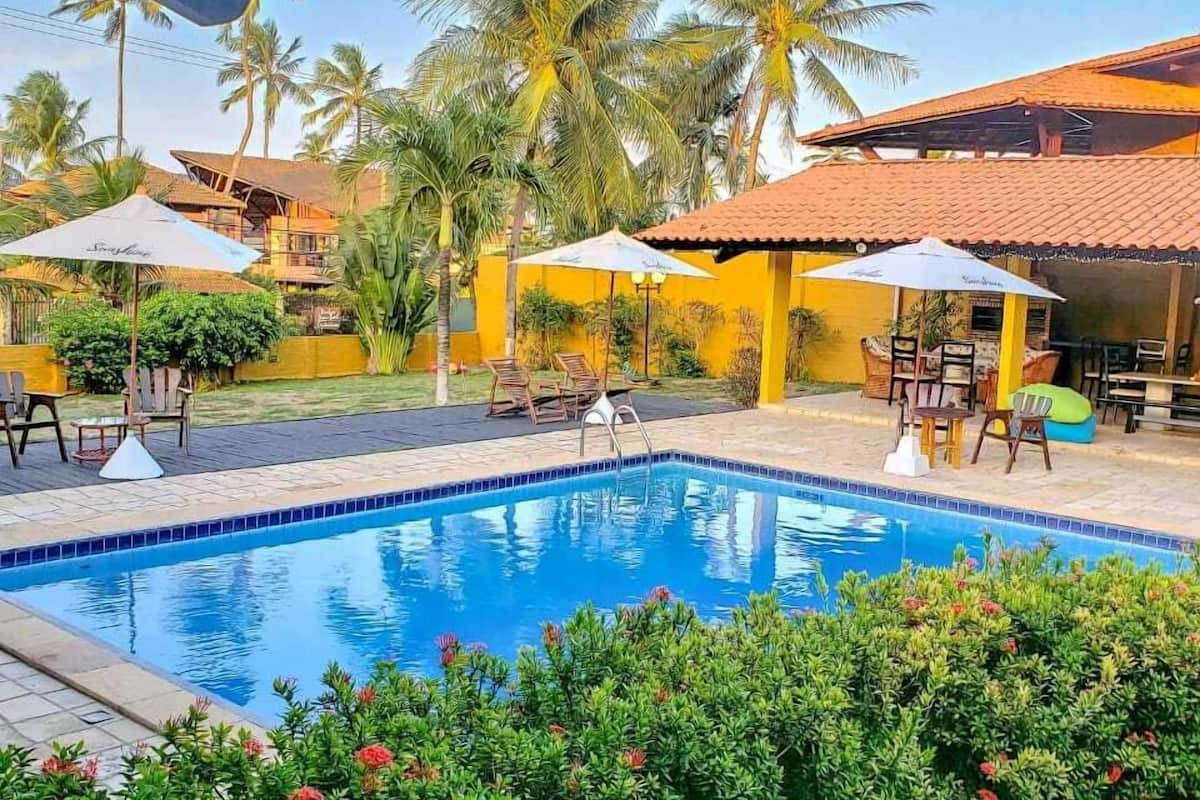 A swimming pool with lounge chairs and umbrellas, surrounded by greenery and palm trees.