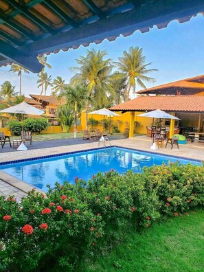 A swimming pool with lounge chairs and umbrellas, surrounded by greenery and palm trees.
