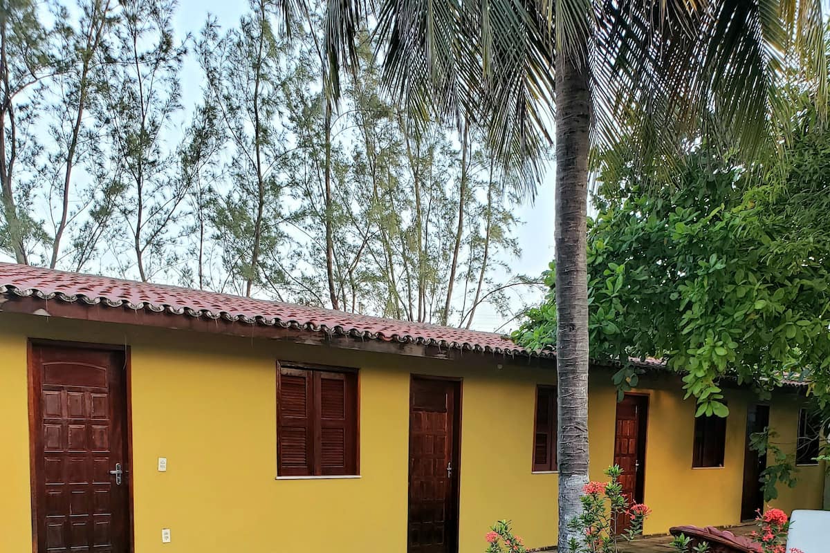 A yellow building with multiple doors and windows, surrounded by a paved area and a small garden with red flowers.