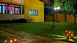 Un edificio amarillo con techo de tejas y una ventana con diseño de cuadrícula. Dos objetos esféricos con diseños de estrella y creciente están sobre el césped.