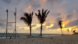 Una playa con palmeras, un arenero y un bote llamado 'KATAVENTO' en la arena.