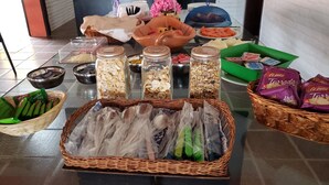 Una mesa de buffet con diversos alimentos, incluyendo tarros de cereales, una cesta de verduras verdes y paquetes de aperitivos.