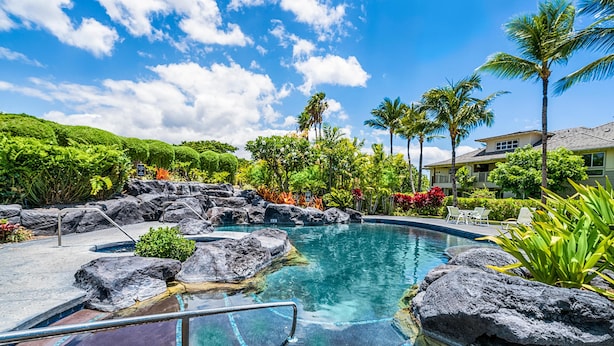 Un ciel d’un bleu éclatant, une piscine bordée de rochers et des plantes tropicales.
