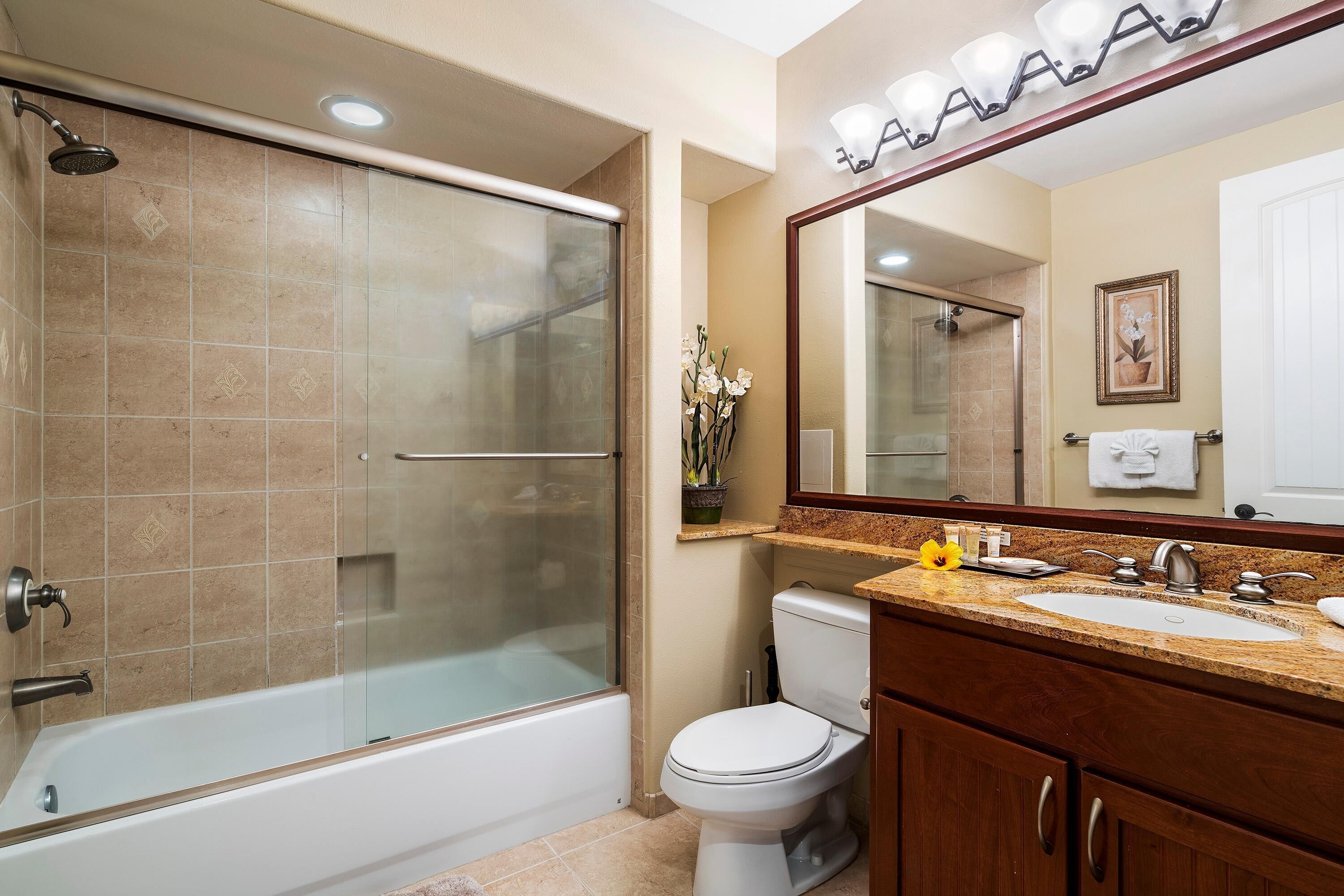 A bathroom with a glass-enclosed shower, a white toilet, and a sink with a mirror above it.