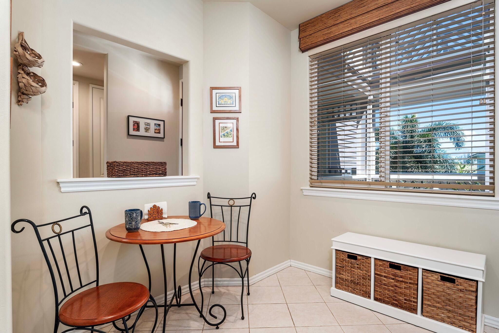 A corner room with a dining table and chairs, a window with blinds, and a white bench with storage baskets.