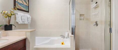Une salle de bain avec une baignoire, une douche et un lavabo. Il y a un tableau encadré au mur, une plante et un porte-serviettes.