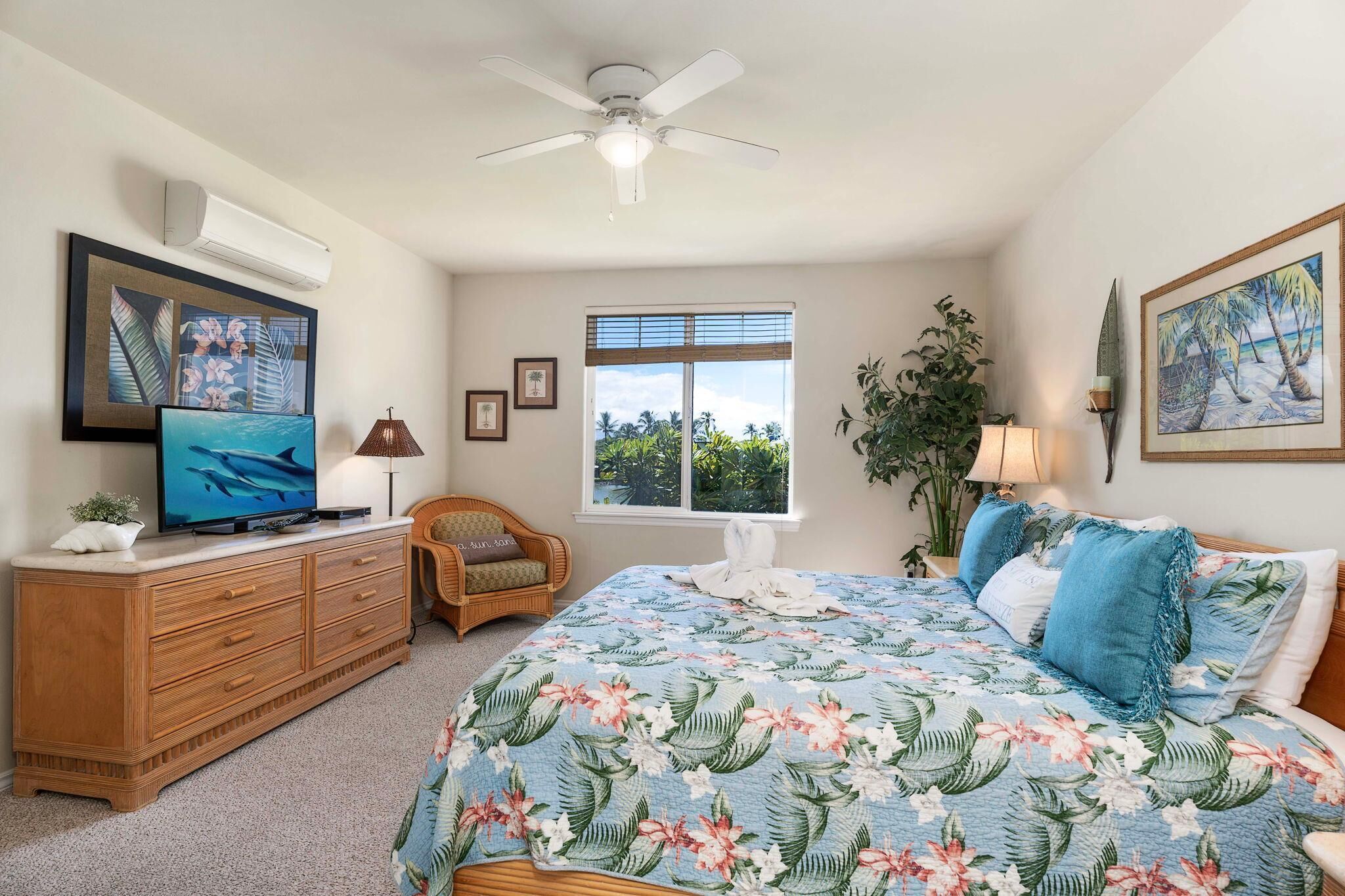 A bedroom with a bed, a television, a dresser, a chair, a window, and a ceiling fan.