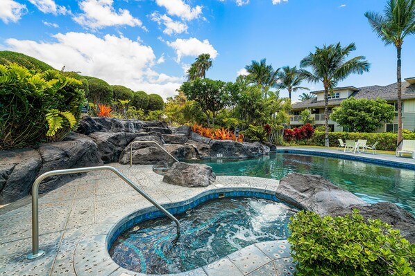 A pool area with a hot tub, surrounded by tropical plants and rocks. - Waikoloa Beach Villas E32 (Waikoloa)