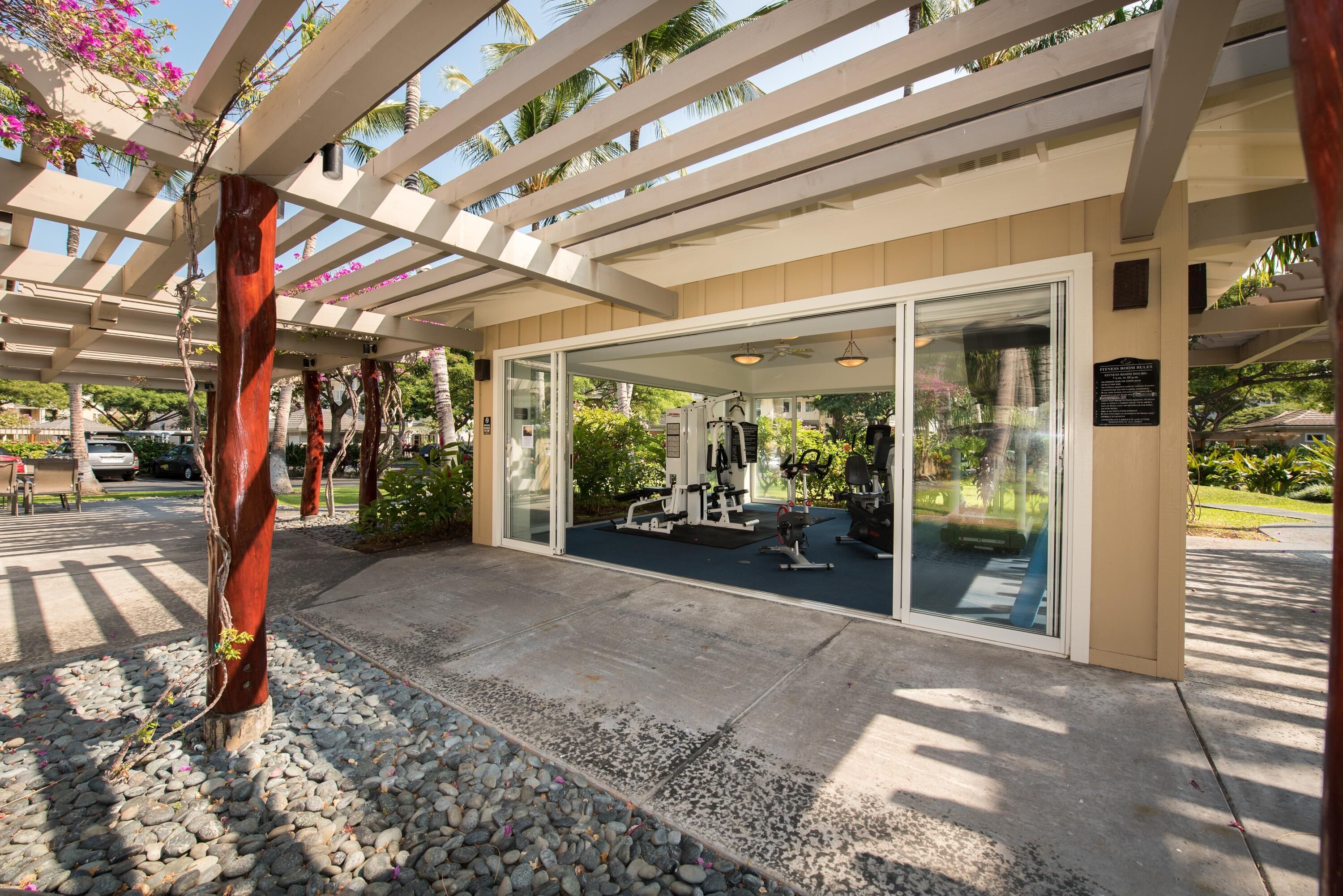 A covered outdoor area with exercise equipment, a glass door entrance, and a pergola structure.