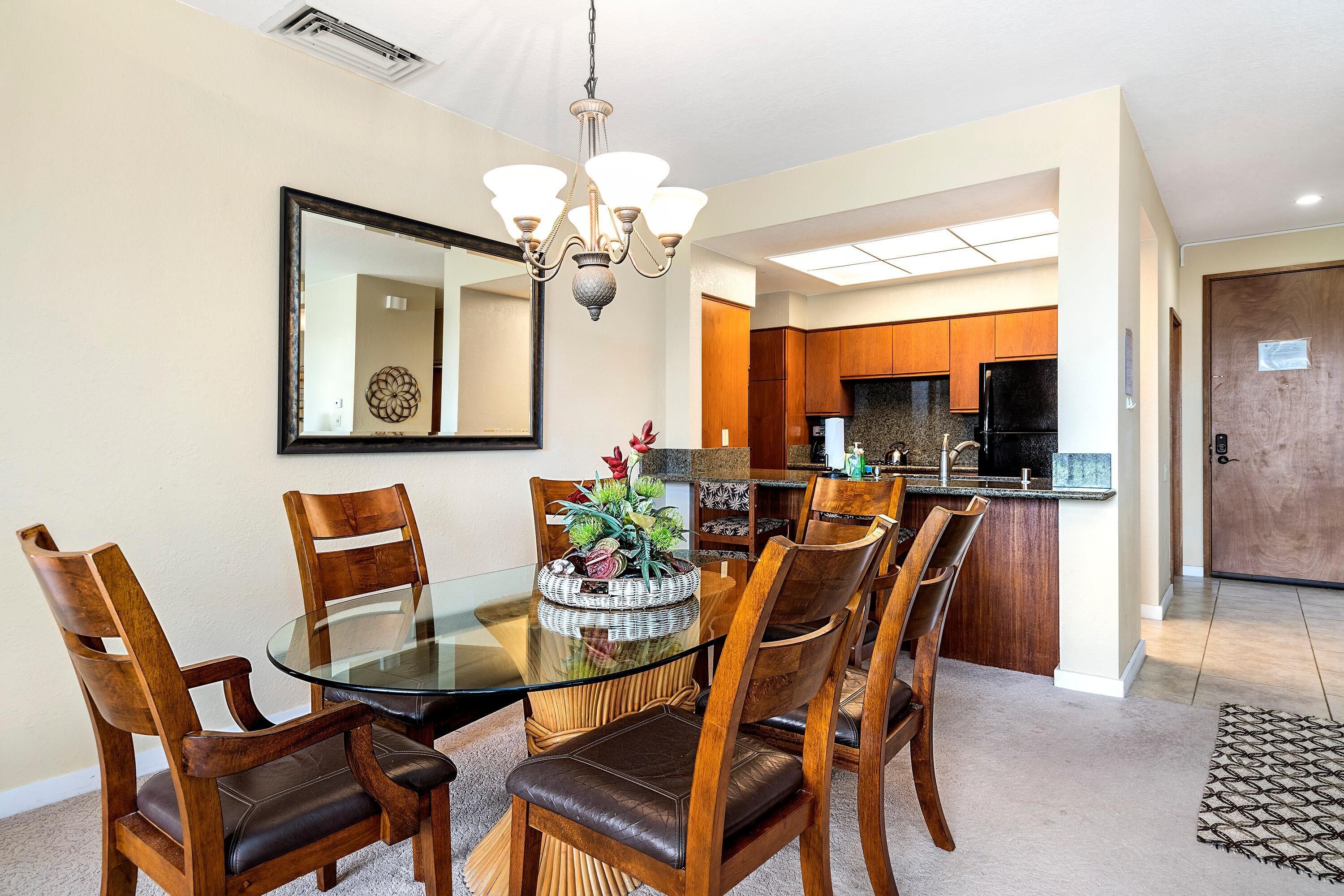 A dining area with a glass table surrounded by wooden chairs, a chandelier, and a decorative centerpiece.