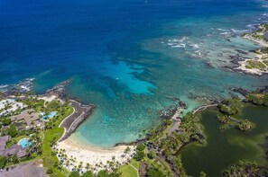 Luchtbeeld van een kustresort met helder turquoise water, een zandstrand en weelderige begroeiing.