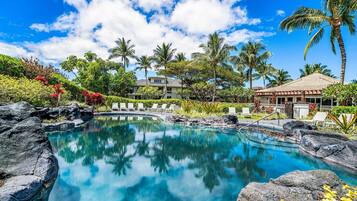 A clear blue pool surrounded by rocks, palm trees, and lounge chairs.