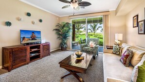 A living room with a TV, wooden entertainment unit, a coffee table, a sofa, and a ceiling fan. - Waikoloa Beach Villas G2 (Waikoloa)