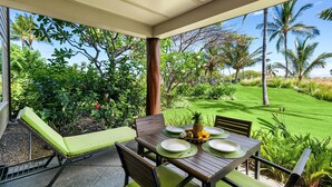 An outdoor patio with a table set for dining, surrounded by lush greenery and palm trees. - Waikoloa Beach Villas G2 (Waikoloa)