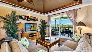 A living room with a sofa, coffee table, TV, and plants. - Waikoloa Beach Villas J32 (Waikoloa)